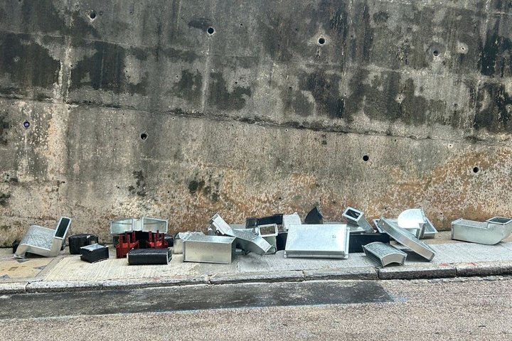 Metallreste von Lüftungsrohren und Ähnlichem liegen auf einem grauen Bürgersteig mit Gefälle vor einer schmutzigen grauen Betonwand 