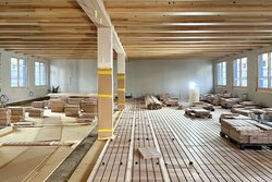 Innenraumfoto eines Holzhauses während dem Bau. Verschiedene Materialien liegen auf dem Boden verteilt, der Boden ist nicht fertiggestellt.