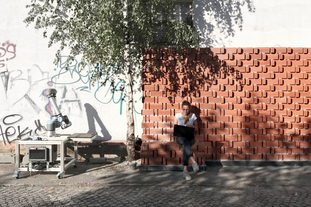 woman with laptop sits in front of "Climate Active Bricks" facade 