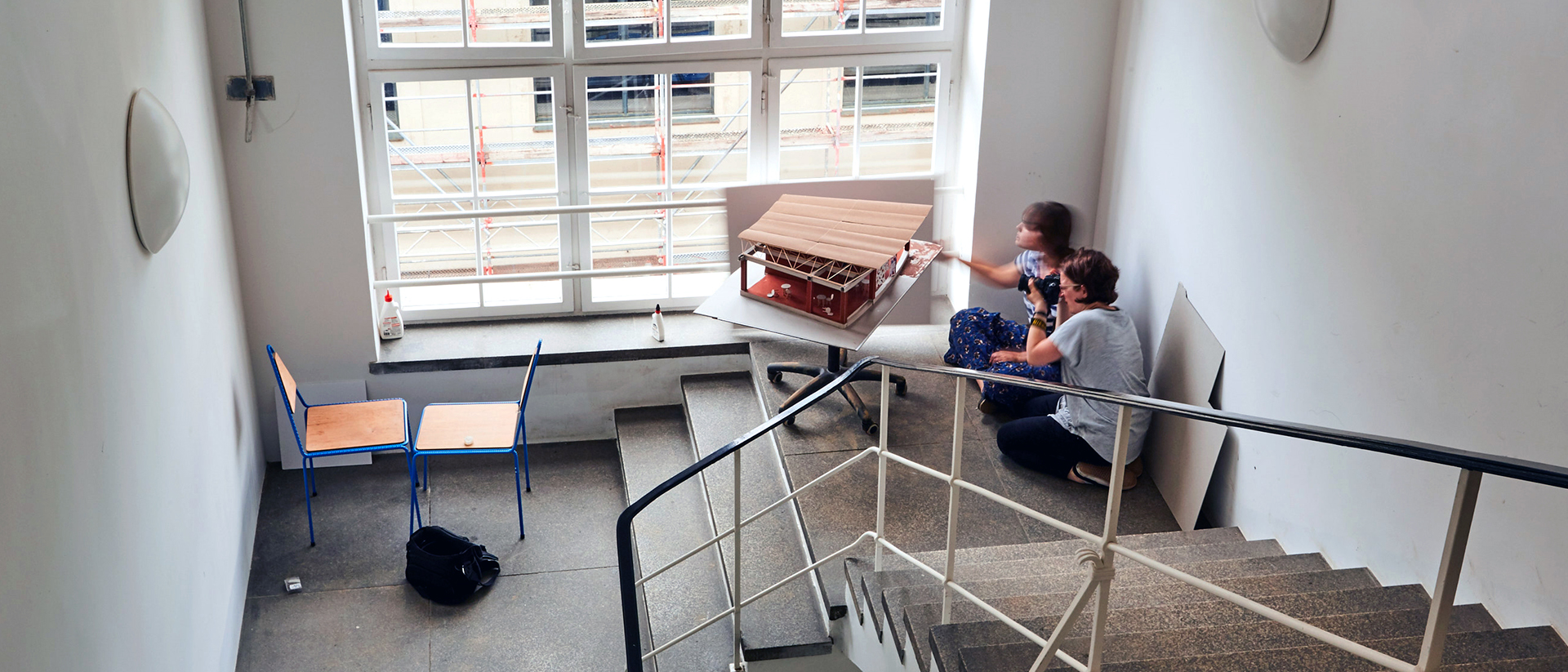 Studierende im Uni-Treppenhaus beim Fotografieren eines Architekturmodells