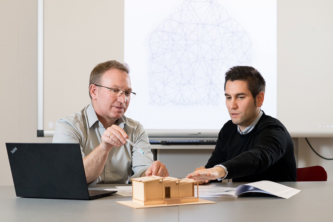 Two researchers in front of computer with architecture model